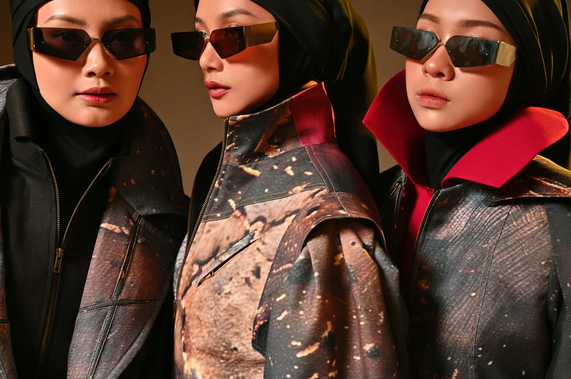 Three hijab models wearing futuristic shield sunglasses and textured acid-wash jackets in studio